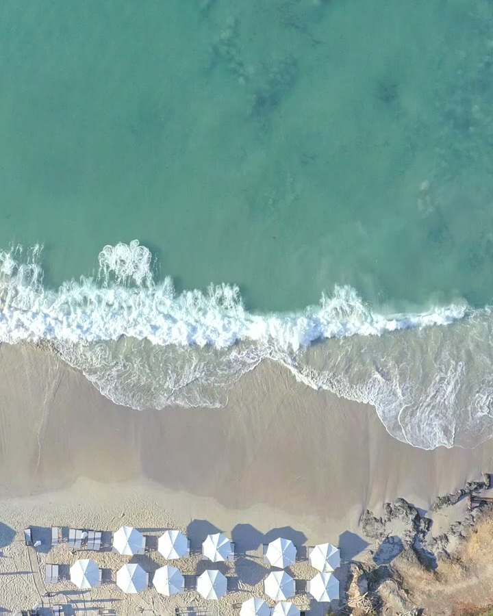 Waves on a beach with white umbrellas, seen from above