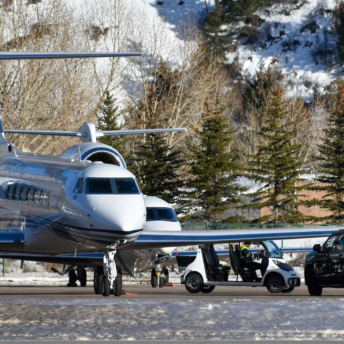Private jets on a snowy mountain apron, cars waiting beside them