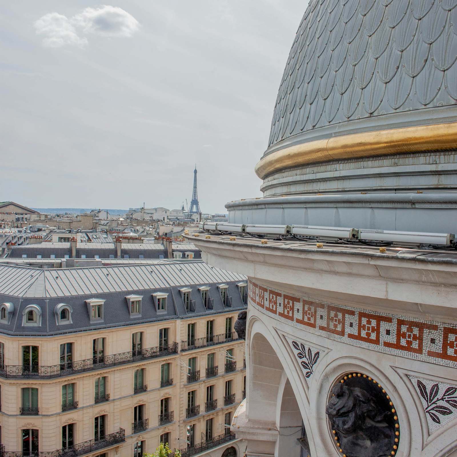 An ornate dome above Haussmann façades, with the Eiffel Tower in the distance