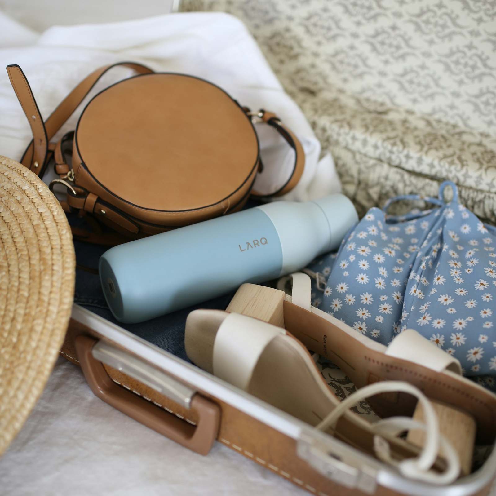 A straw hat, a leather bag and summer clothes packed for a journey